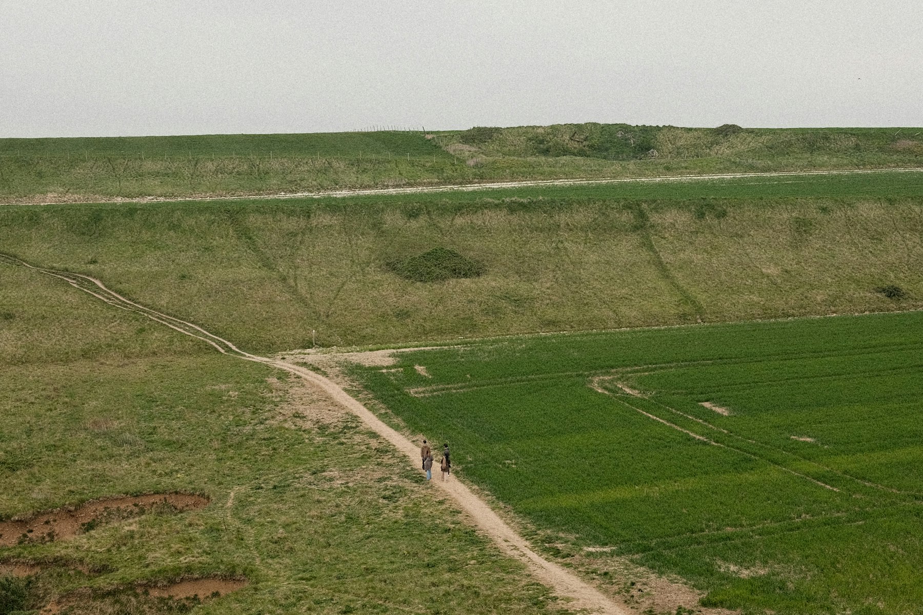Two people walking a dirt path through grassy hills